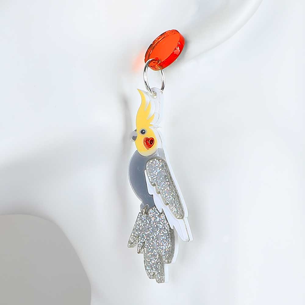 Cockatoo dented diva earrings. Acrylic cockatoo hangs from orange mirror disc ear stud. Photographed on white background for Australian Museum Shop online