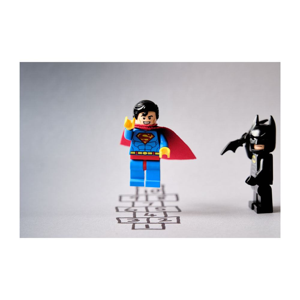 Two LEGO figures, one resembling Superman and the other Batman, standing on a gray surface with a white background.