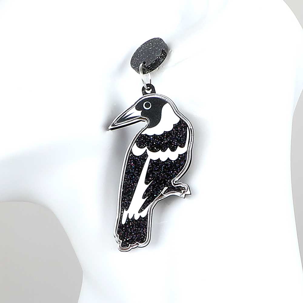 Magpie dented diva earrings. Acrylic magpie hangs fromblack sparkle disc ear stud. Photographed on white background for Australian Museum Shop online
