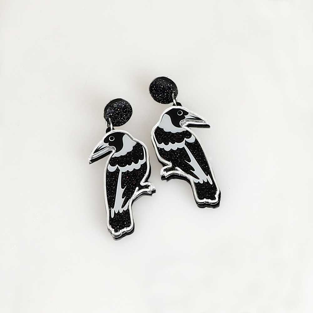 Magpie dented diva earrings. Acrylic magpie hangs from black sparkle disc ear stud. Photographed on white background for Australian Museum Shop online