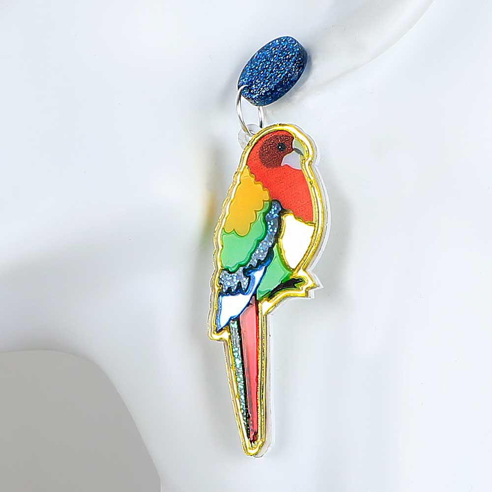 Rosella dented diva earrings. Acrylic rosella hangs from blue sparkle disc ear stud. Photographed on white background for Australian Museum Shop online