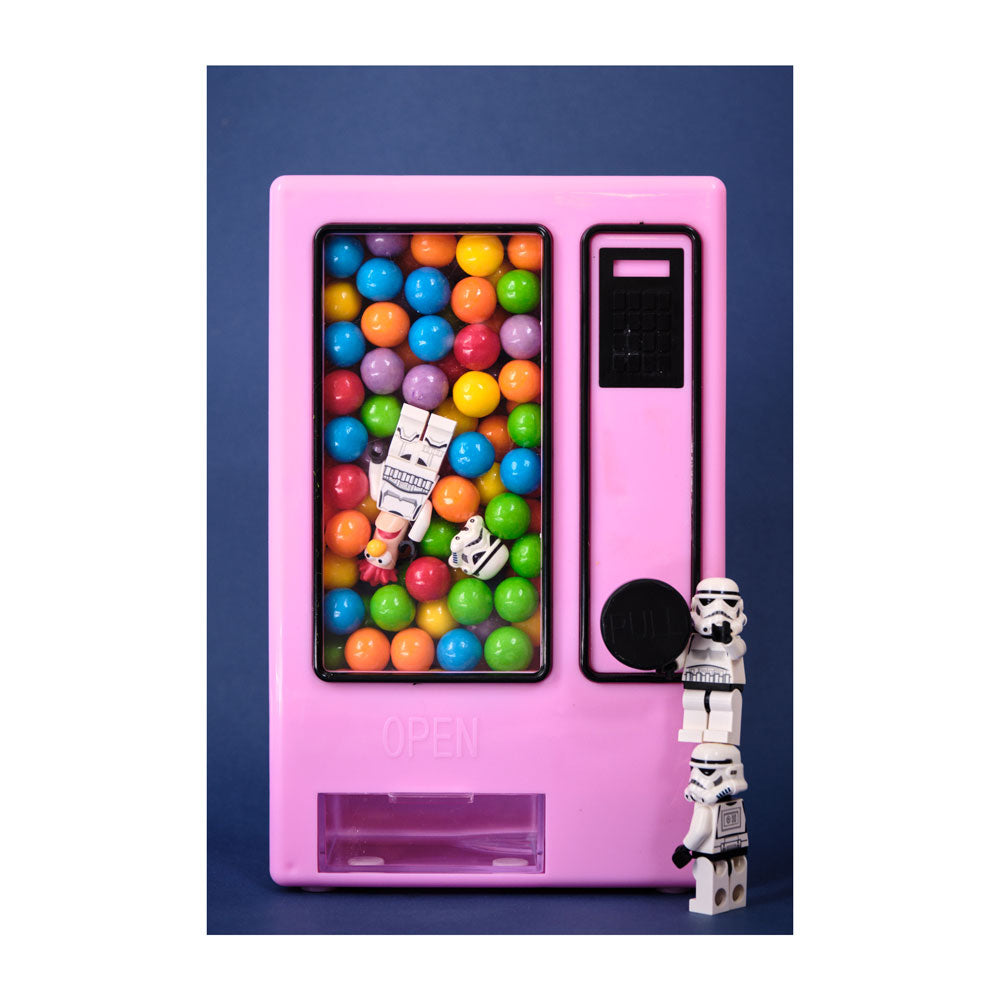 Pink gumball machine with colorful gumballs and a stormtrooper figure on a blue background. Adam Popovic photographic print for Relics exhibition on white background