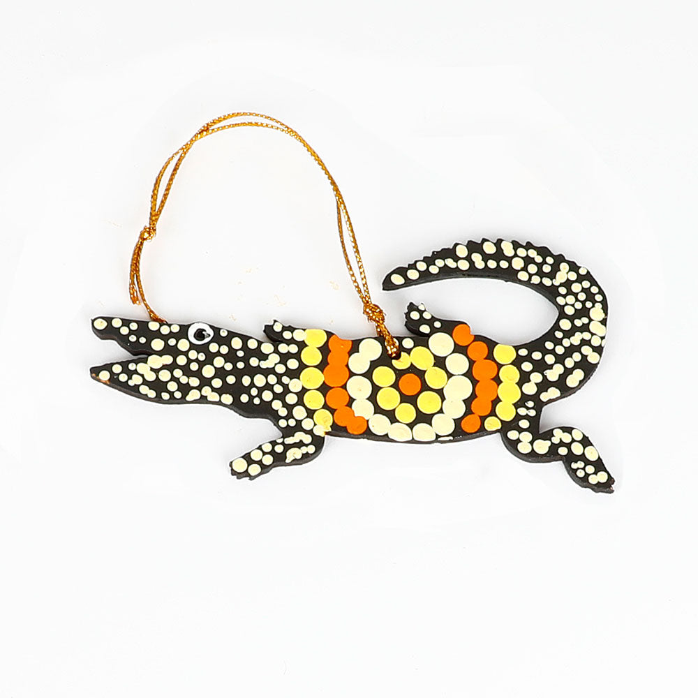 Decorative crocodile ornament from Warlukurlangu artists cooperative, with orange and yellow black and white pattern on a white background